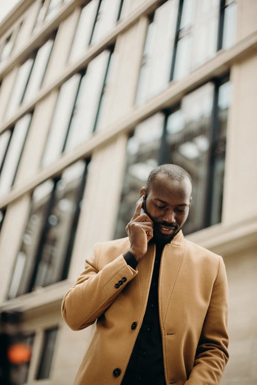 选择性聚焦低角度照片的棕色外套的男人谈到背景的电话机智大厦 · 免费素材图片