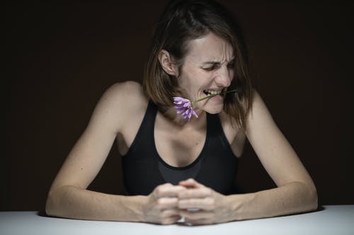 黑色背心咬紫色花瓣花的女人 · 免费素材图片