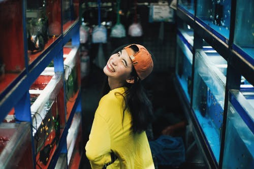 鱼缸摆在黄色上衣和橙色帽子的微笑女人的照片 · 免费素材图片