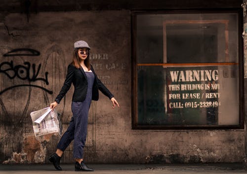 女人拿着报纸走在人行道上的照片 · 免费素材图片