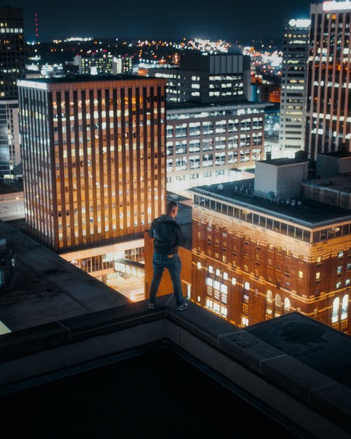 穿黑夹克的男人站在建筑物的边缘 · 免费素材图片
