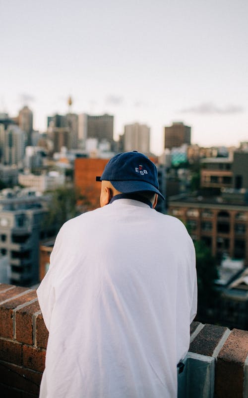 男人穿着白衬衫和蓝色的帽子，看着建筑物 · 免费素材图片