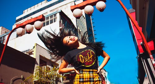 黑色和黄色的圆领t恤站在棕色和白色的混凝土建筑附近的女孩 · 免费素材图片