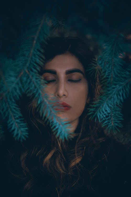 一个女人的特写镜头闭着眼睛被叶子包围 · 免费素材图片