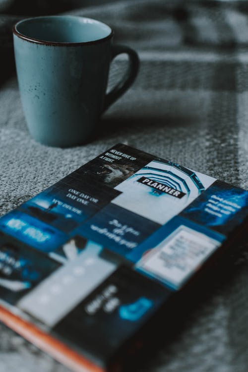 桌上的陶瓷杯旁边的蓝色和黑色计划器 · 免费素材图片