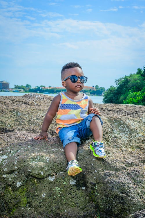 男孩戴着墨镜坐在岩石上 · 免费素材图片