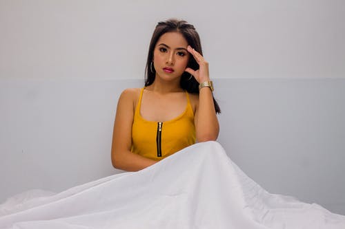 女人穿着黄色意大利面条皮带顶抱着她的脸 · 免费素材图片