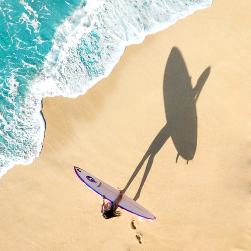 按住白色和紫色的冲浪板在海边散步的女人 · 免费素材图片