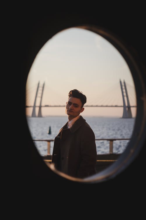 穿黑夹克的男子站在水的附近 · 免费素材图片