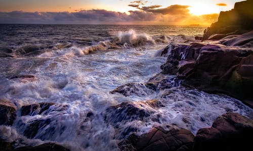 海浪在日落时撞在岩石上 · 免费素材图片