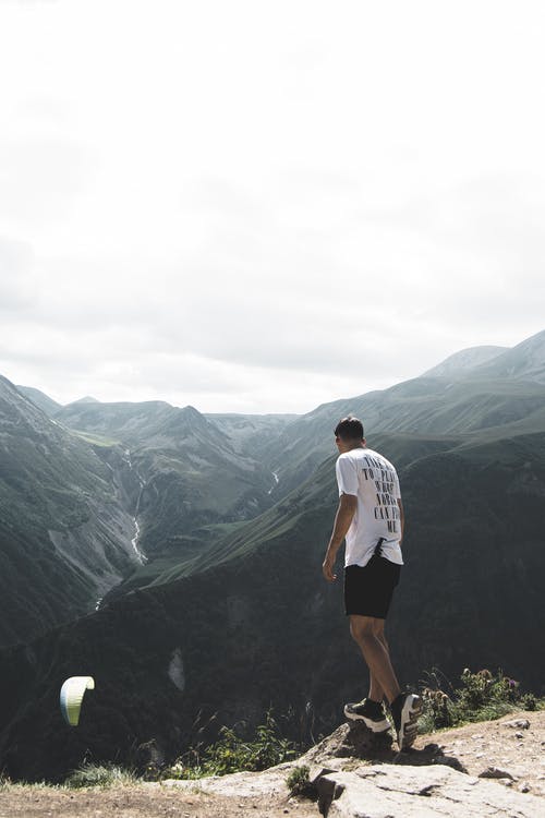 身穿白色t恤和黑色短裤站在悬崖上的男人 · 免费素材图片