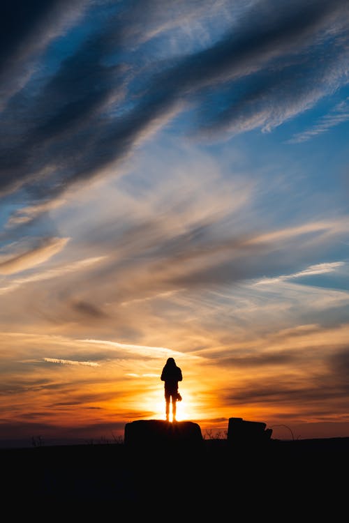 一个人站在一块岩石上的剪影 · 免费素材图片