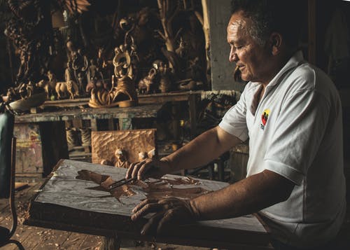 在木制雕塑上工作的白色polo衫的男人 · 免费素材图片
