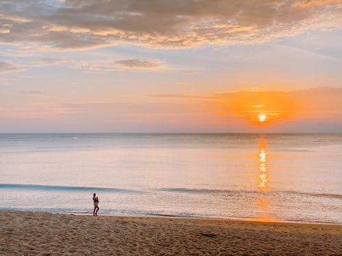 2人在日落时在海滩上行走 · 免费素材图片