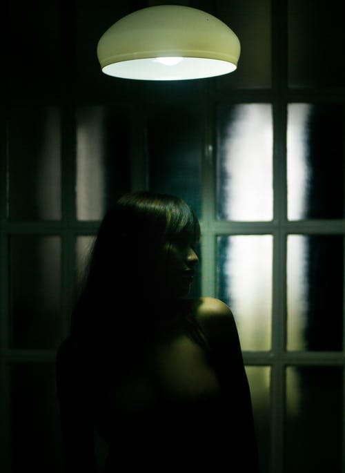 在黑暗的房间里的电灯下的苗条女人 · 免费素材图片