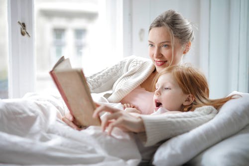 母亲和女儿在床上感兴趣的阅读书 · 免费素材图片