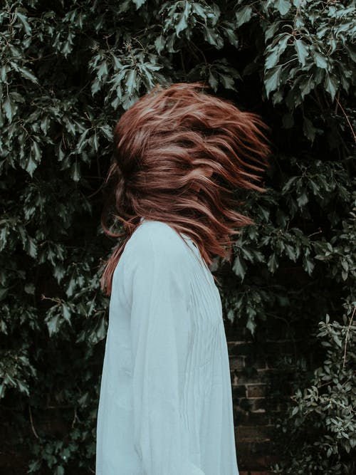 女人穿着白色长袖连衣裙站在附近绿叶植物做头发翻转的侧视图照片 · 免费素材图片