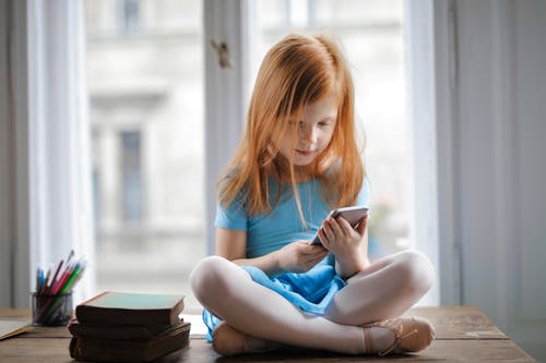 安静的小姜女孩坐在桌子上，在明亮的客厅里使用智能手机 · 免费素材图片