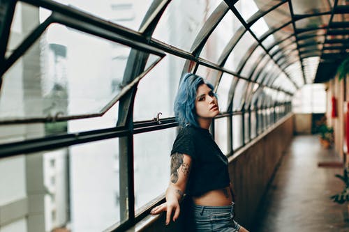 蓝头发的女人，穿着黑色衬衫和蓝色牛仔短裤，站在空旷的走廊上的选择性焦点照片 · 免费素材图片