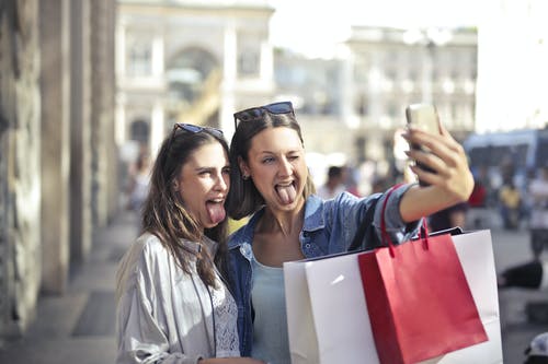 性格开朗的年轻女性，与采取在大街上的自拍照的购物袋 · 免费素材图片