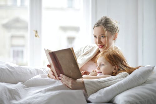 躺在床上微笑的母亲和女儿读书的照片 · 免费素材图片