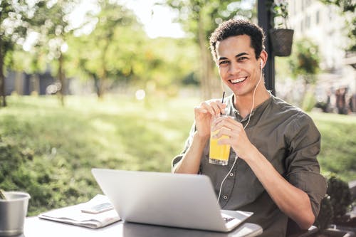 快乐的人坐在一起的笔记本电脑和果汁在公园 · 免费素材图片