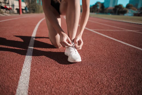 女人在跑道上绑她的白色运动鞋的特写照片 · 免费素材图片
