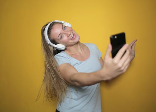 在白色的背心，同时自拍照听音乐的耳机微笑的女人的照片 · 免费素材图片