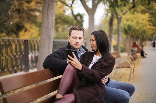 夫妻坐在棕色的木凳上，看着电话的选择性聚焦照片 · 免费素材图片