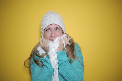 蓝色针织毛衫，白色针织无檐小便帽和白色围巾微笑的女人的肖像照片 · 免费素材图片