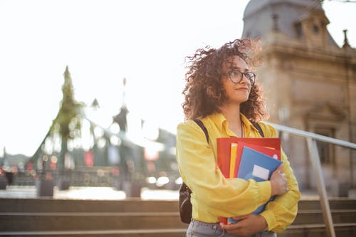 女人在黄色的长袖衬衫和眼镜携带文件夹中的选择性焦点照片 · 免费素材图片