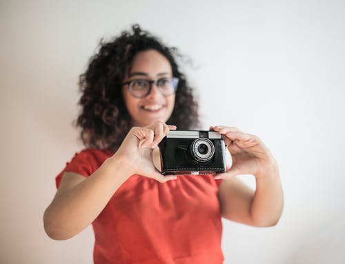 红顶伸出一个黑色相机的微笑女人的选择性焦点照片 · 免费素材图片