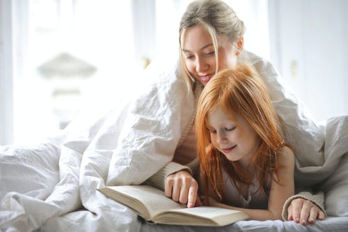 母亲和女儿在床上读书的照片 · 免费素材图片