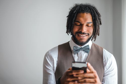 白色礼服衬衫和棕色waistcoat Texting的男人微笑着的肖像照片 · 免费素材图片
