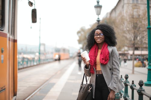 灰色的外套和黑色的裤子，站在电车旁边的微笑妇女的选择性聚焦照片 · 免费素材图片