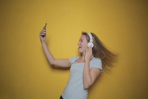 白色背心的微笑妇女的侧视图照片采取自拍照时在耳机上听音乐的 · 免费素材图片