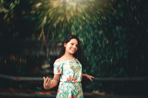 小女孩微笑着花裙子站在栏杆上的选择性焦点照片 · 免费素材图片