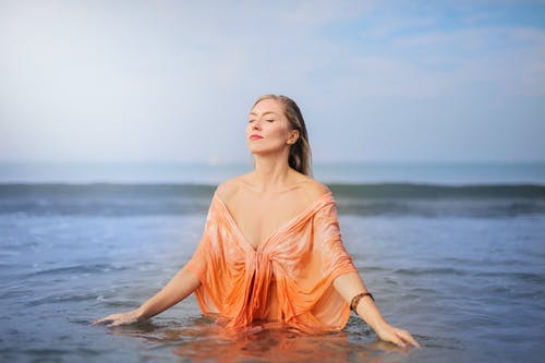 闭着眼睛在水体中的橙色上衣的女人 · 免费素材图片