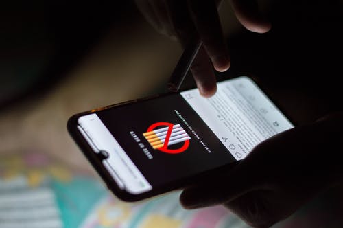 拿着香烟时使用智能手机的人的选择性焦点特写照片 · 免费素材图片