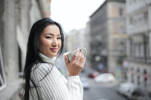拿着白色杯子的白色编织毛线衣的妇女选择聚焦照片 · 免费素材图片