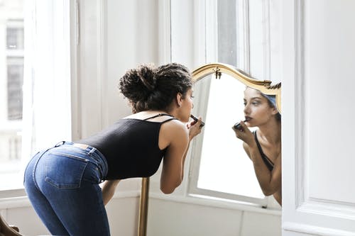 黑色背心和蓝色牛仔布在镜子前应用口红的女人的照片 · 免费素材图片