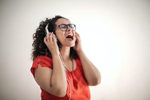 红顶和黑框眼镜在她的耳机上听音乐的唱歌女人的照片 · 免费素材图片