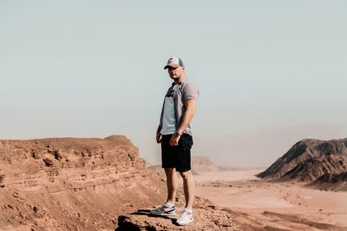 男子站在沙漠中的岩层上 · 免费素材图片