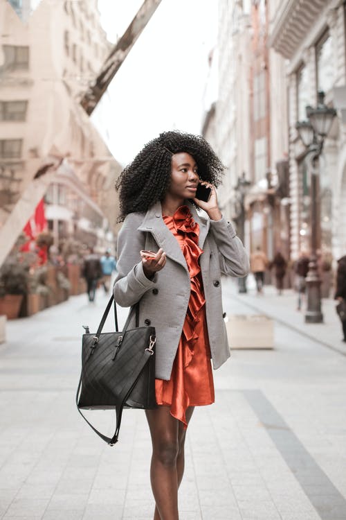女人穿着灰色外套，拿着墨镜，并在电话上交谈时携带黑色皮包的选择性聚焦照片 · 免费素材图片