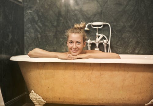 坐在白色陶瓷浴缸的微笑妇女的照片 · 免费素材图片
