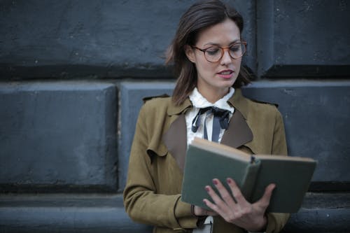 棕色外套和眼镜看书的女人的照片 · 免费素材图片