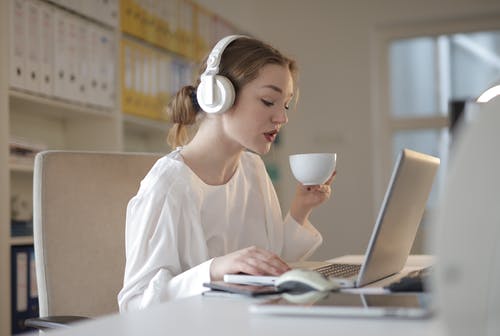女人在喝咖啡和使用她的笔记本电脑时听音乐的耳机的选择性聚焦照片 · 免费素材图片