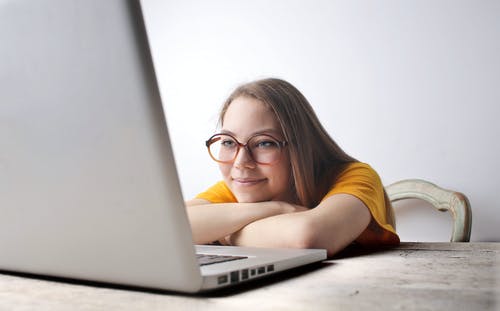 一件黄色的衬衫，看着她的笔记本电脑的微笑女人的照片 · 免费素材图片