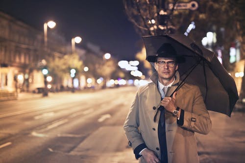 戴黑帽子和棕色大衣的人在人行道上行走时拿着伞的选择性聚焦照片 · 免费素材图片