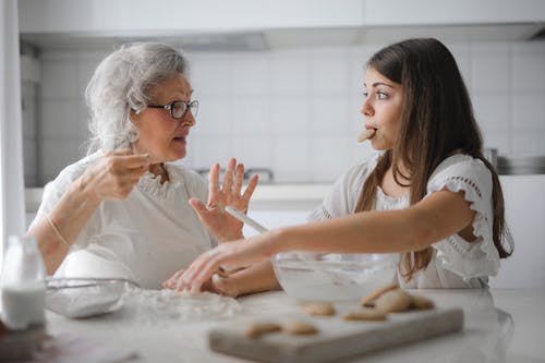 沉思的祖母和孙女一起在明亮的现代厨房做饭时有趣的谈话 · 免费素材图片